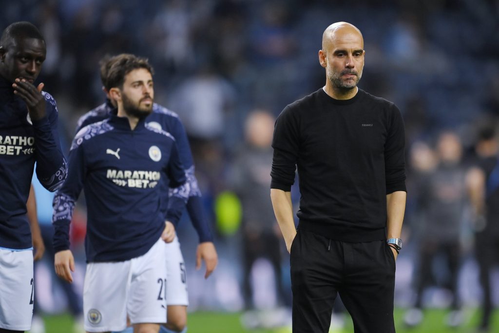 Treinador Pep Guardiola de mãos nos bolsos e atrás jogadores do Manchester city